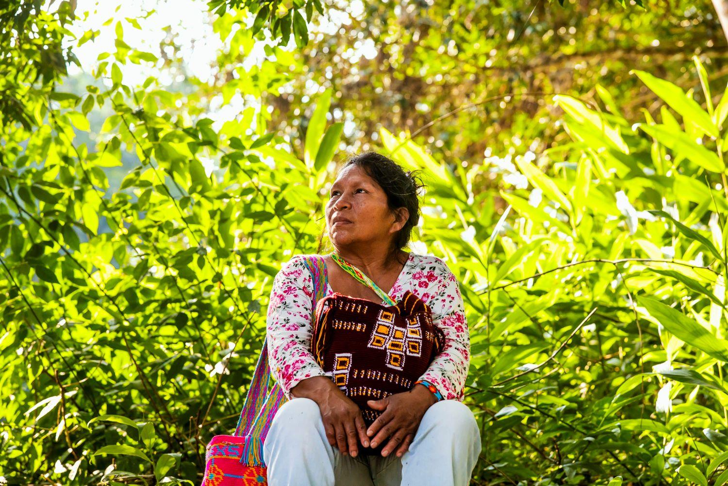 A woman in Colombia sits in front of greenery and looks into the distance. Photo: UN Women/Juan Camilo Arias